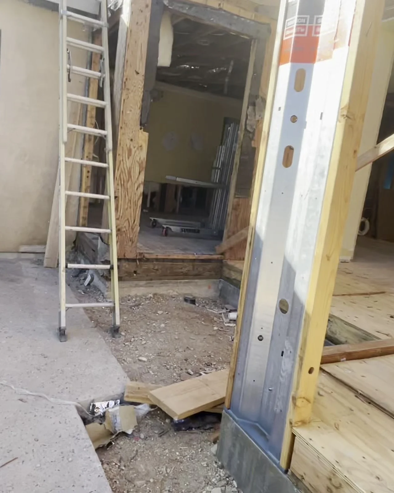 The main level opened up to raw framing — a ladder against the studs, an opening sheeted over for protection, offcuts across the subfloor