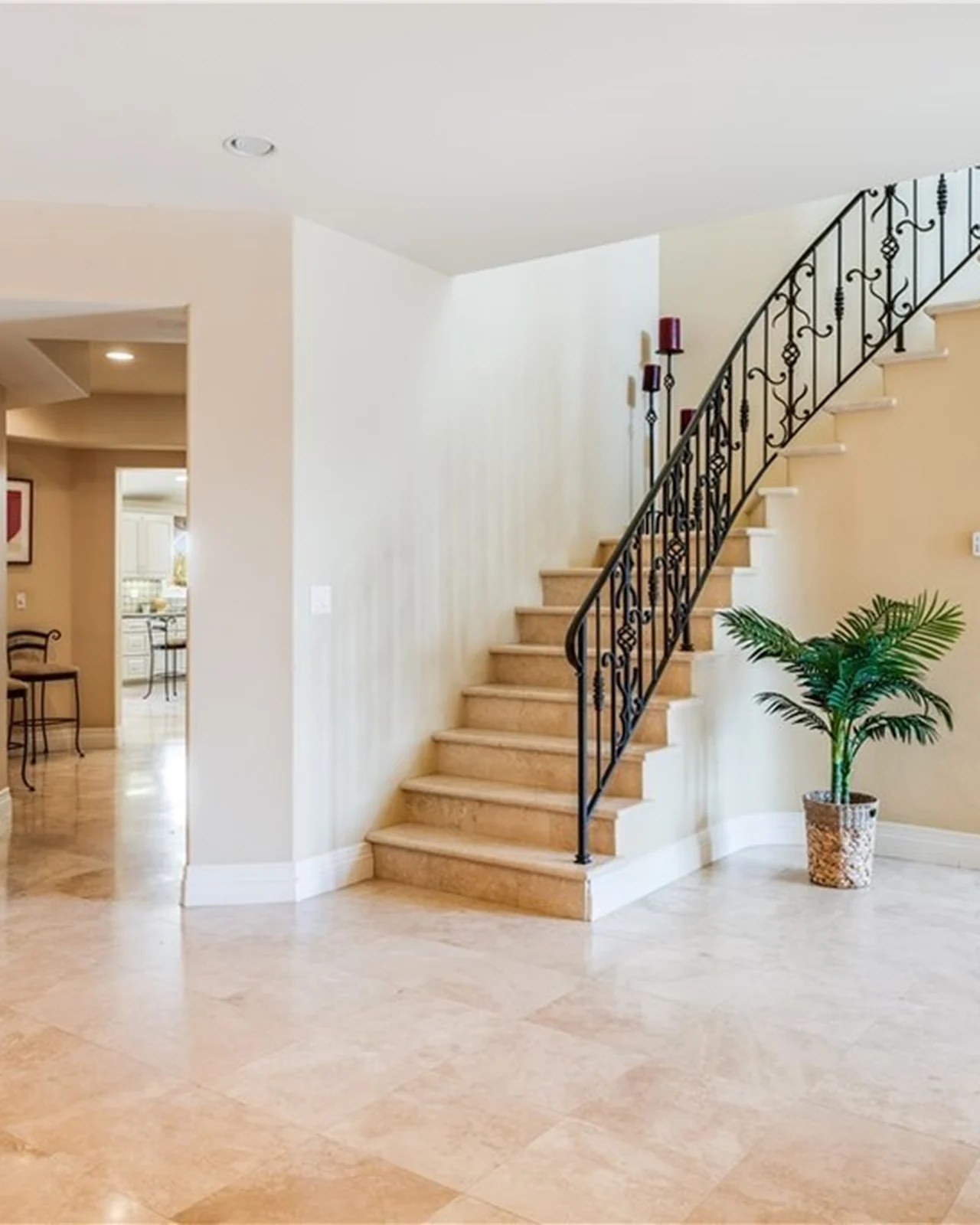 Original entry and stair hall with a travertine floor, a curved staircase with scrolled wrought-iron balusters, beige walls and a potted palm