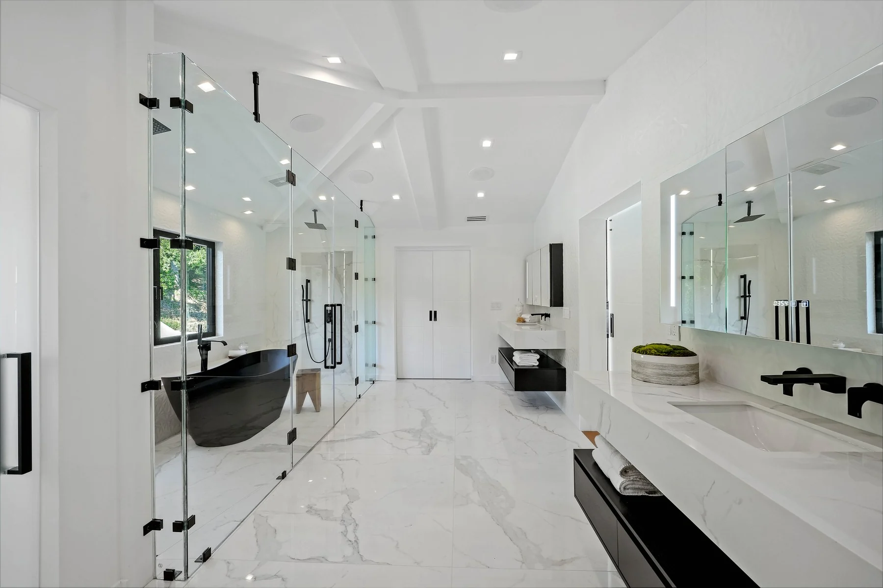Wide view of the marble bathroom with slab walls, a freestanding tub and a frameless glass enclosure