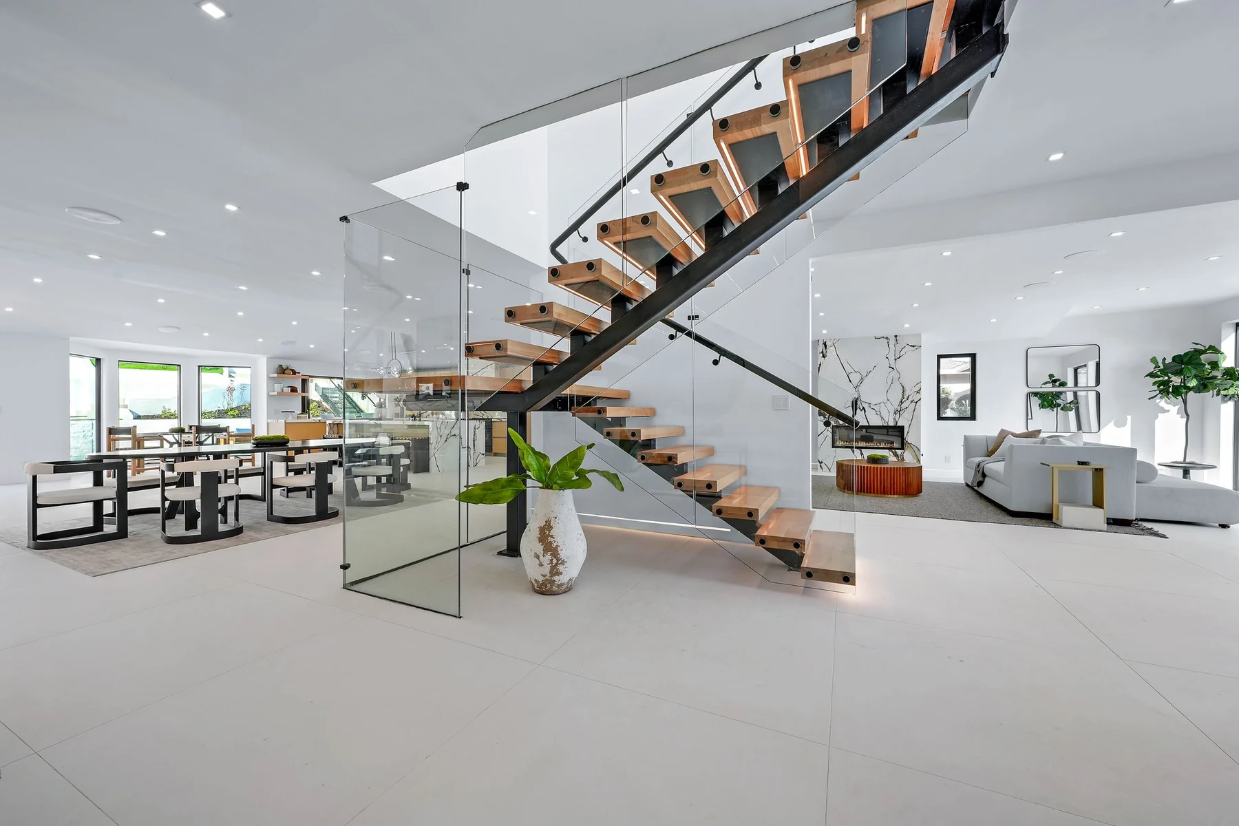Wide view across the open plan to the open-riser oak stair with its frameless glass guard